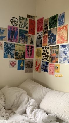 an unmade bed with white sheets and posters on the wall