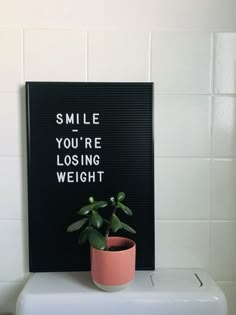 a sign that says smile you're losing weight next to a potted plant