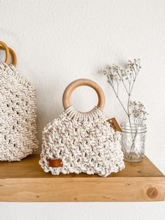 two crocheted bags sitting on top of a wooden shelf next to vases