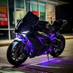 a motorcycle is parked on the street in front of a building with purple lights around it