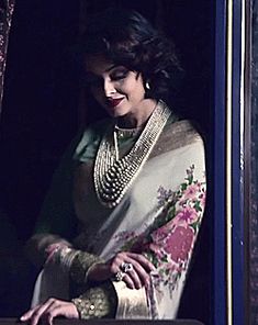 a woman in a white sari is looking out the window with her hand on top of a suitcase