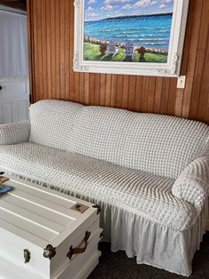 a white couch sitting next to a wooden wall with a painting on the wall above it