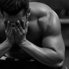 a man with his hands on his face sitting in front of a mirror looking down