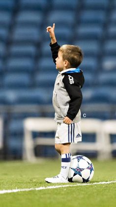 a young boy standing on top of a soccer field holding a soccer ball in his hand