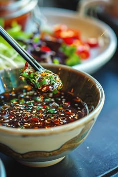 a bowl full of soup with chopsticks sticking out of it and salad in the background