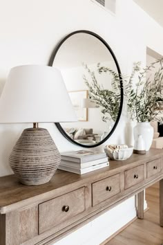 a table with a lamp and mirror on it next to a dresser in a living room