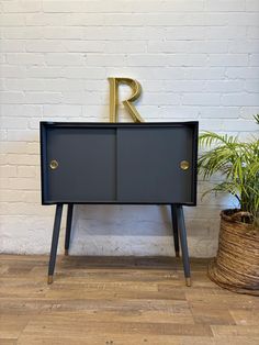 the letter r is placed on top of a black cabinet next to a potted plant