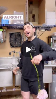 a man holding a flower in his hand and laughing at the camera while standing next to a kitchen sink