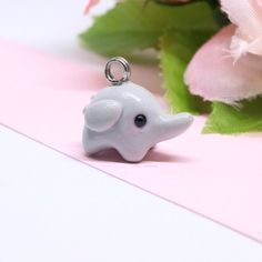 a white elephant keychain sitting on top of a pink table next to flowers