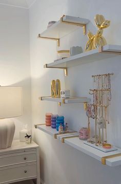 a white shelf with gold decorations on it in a room next to a dresser and lamp