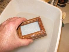 a hand holding a small wooden frame in a white bowl on top of a table