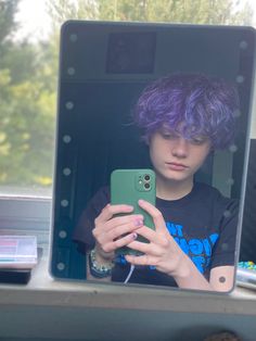 a girl with purple hair is looking at her cell phone in front of a mirror