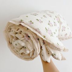 a woman's hand holding up a white and pink flowered blanket on top of her head