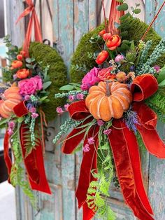 two wreaths hanging on the side of a wooden door decorated with flowers and foliage