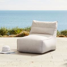 an outdoor lounge chair with a hat on the ground next to it and water in the background