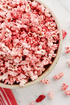 a bowl filled with pink popcorn on top of a white marble counter next to red and white striped napkins