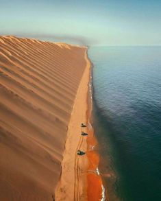 an aerial view of the ocean and sand dunes near a beach with cars parked on it