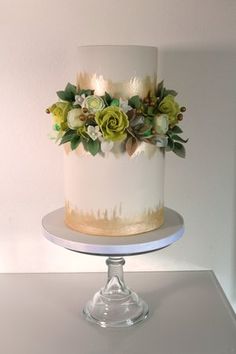 a white and gold cake with flowers on top sitting on a table next to a wall