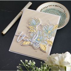 a close up of a card on a table next to flowers and a plate with a pen