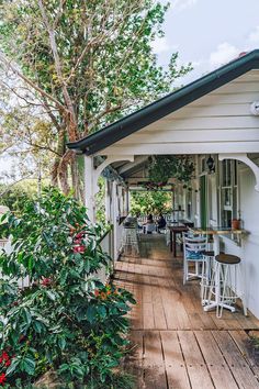 an outdoor restaurant with tables and chairs on the porch next to some trees, bushes and flowers