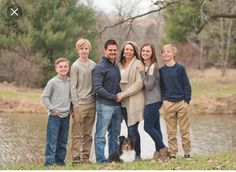 a family poses with their dog in front of a pond