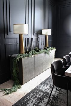 an elegant dining room with black walls and wooden flooring, decorated with greenery