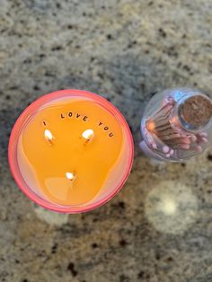 an orange candle with i love you written on it next to a small glass jar