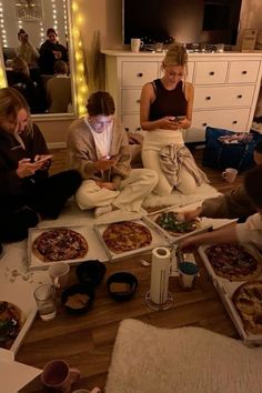 several people sitting on the floor in front of pizzas and cell phones, all looking at their phones