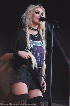 a woman with long blonde hair standing in front of a microphone and wearing black boots