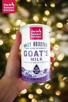 someone holding up a can of goat's milk in front of a christmas tree