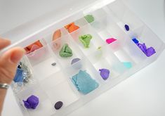 a person holding a plastic container filled with different types of colored rocks and stones in it