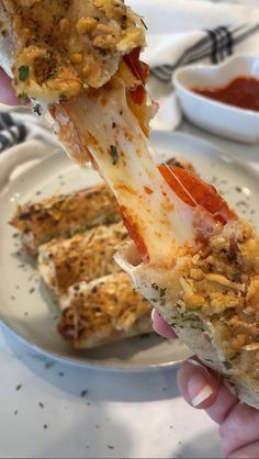 a person holding up a piece of pizza on a plate with sauces and condiments in the background