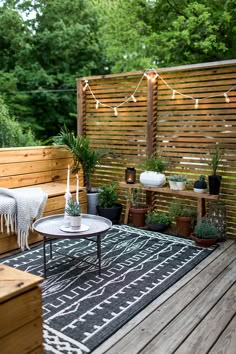 an outdoor deck with potted plants and lights strung on the fence behind it,