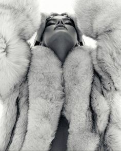 a black and white photo of a woman in fur coat with her hands on her head