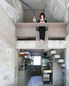 a woman sitting on the ledge of a loft above a kitchen and dining room area