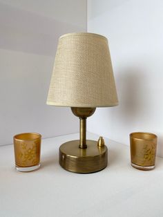 a lamp, two cups and a candle holder on a white tablecloth covered surface