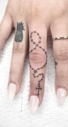 a person with tattoos on their fingers and hand holding a cross, pineapple and rosary