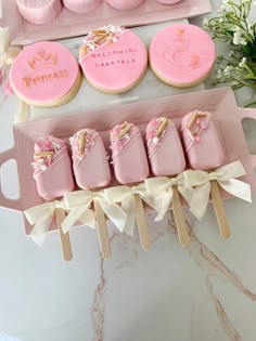 pink decorated cookies and cupcakes are displayed on trays with ribbon around them