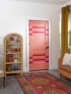 a living room filled with furniture and a pink door next to a book shelf on top of a rug