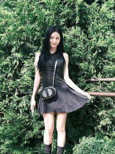 a woman standing in front of some bushes holding a purse and posing for the camera