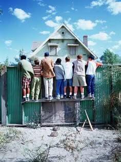 a group of people standing on top of a green fence next to a small house