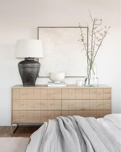 a bedroom with a bed, dresser and vases on top of the dresser in front of it