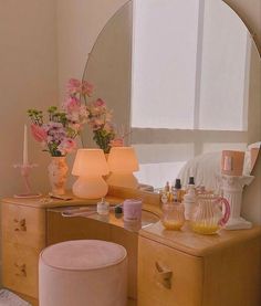 a vanity with flowers and candles on it in front of a large round mirror over a bed