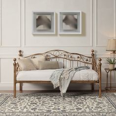 a white bed with two pictures on the wall above it and a rug in front of it