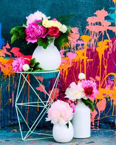 two white vases with pink and yellow flowers in front of a colorful wall background