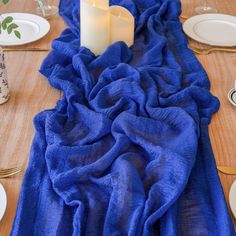 a blue table runner with two white candles on it and place settings in the background