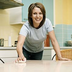 a woman is smiling while cleaning the kitchen table with a mop and duster