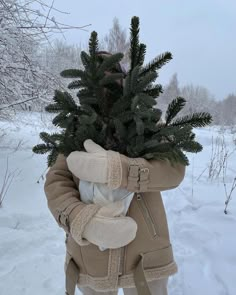 a person holding a small tree in their arms while standing in the snow with it's hood up