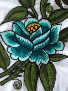 a blue flower with green leaves on a white shirt that has yellow dots in the center