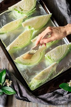 someone using a knife to cut lettuce into wedges on a baking sheet